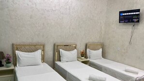 Habitación de hotel con tres camas individuales, un televisor montado en la pared y una mesita con un jarrón de flores.