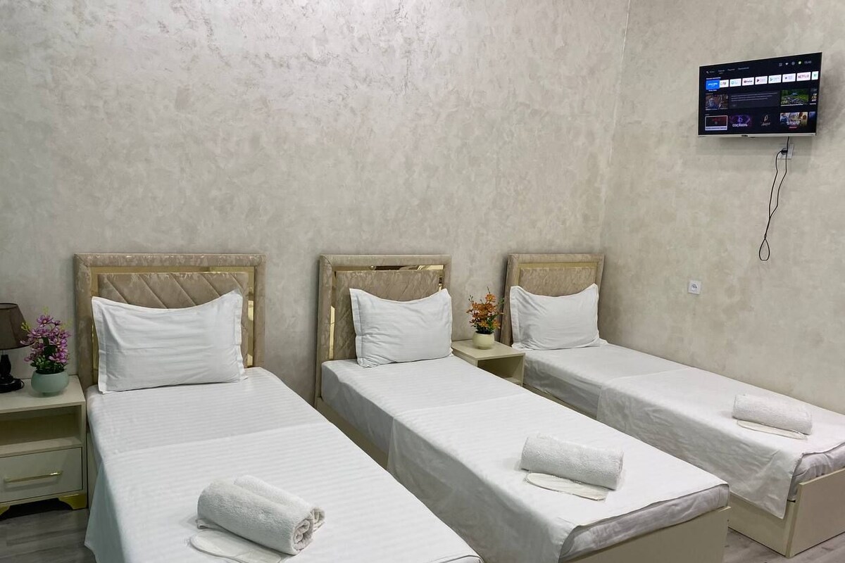 A hotel room with three single beds, a TV mounted on the wall, and a small table with a vase of flowers.