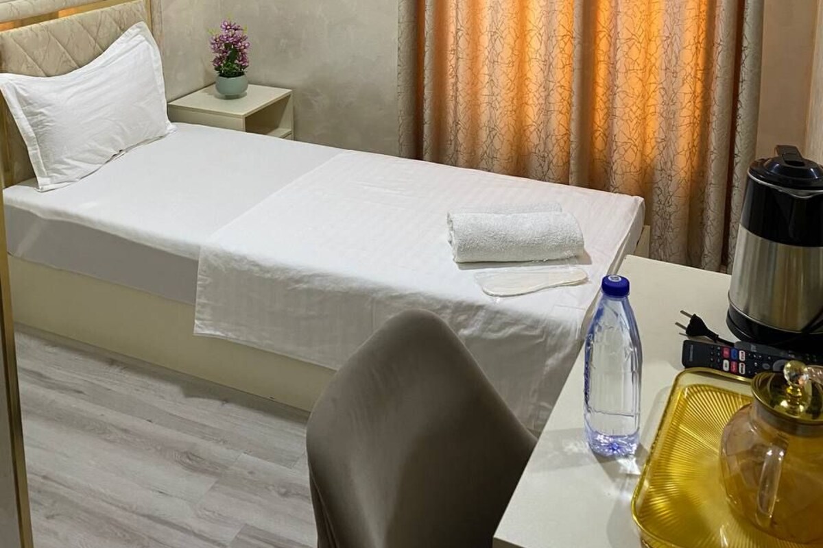 A hotel room with a bed, a bedside table with a lamp, a water bottle, and a power strip.