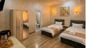 Habitación de hotel con dos camas, un escritorio con cafetera, televisión y baño visible a través de una puerta.