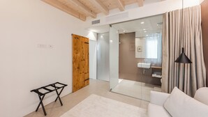 Ein modernes Interieur mit Holzboden, einer Glastür zu einem Badezimmer, einem schwarzen Tisch und einem weißen Sofa.