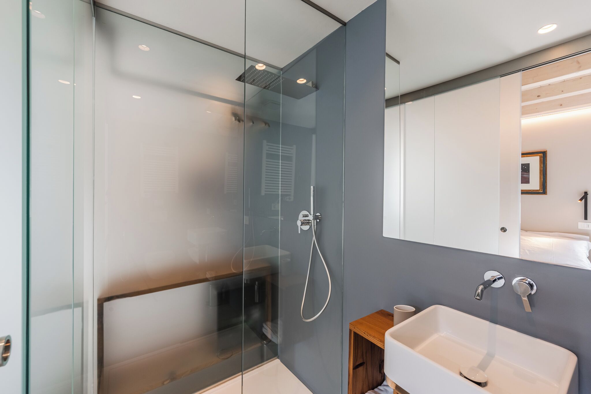 A modern bathroom with a glass shower enclosure, a white sink, and a wooden cabinet.