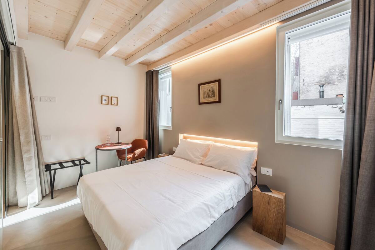 A bedroom with a bed, a desk, a chair, a window, and a picture on the wall.