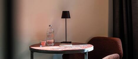 A hotel room with a bed, a small table with a lamp, a chair, and two framed pictures on the wall.
