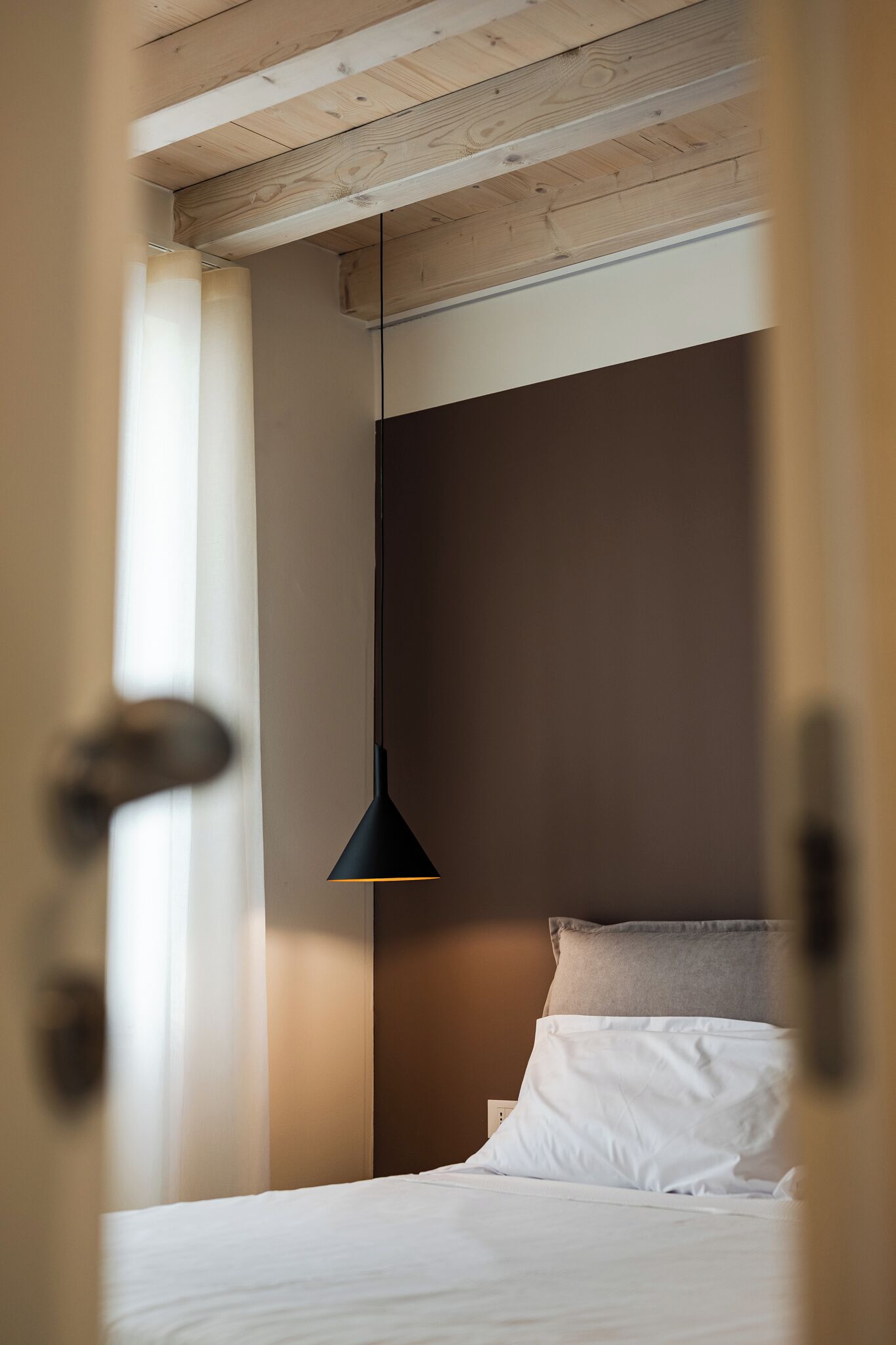 A bedroom with a bed, a hanging light fixture, and a wooden ceiling.