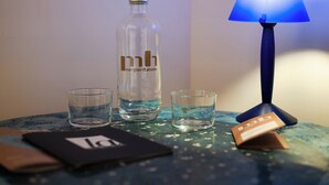 Eine mit 'mh' beschriftete Flasche und drei Gläser auf einem Tisch mit einer blauen Lampe.