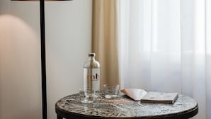 Ein runder Tisch mit einer Glasflasche, einem Glas, einem Buch, einer schwarzen Lampe und zwei gerahmten Bildern an der Wand.