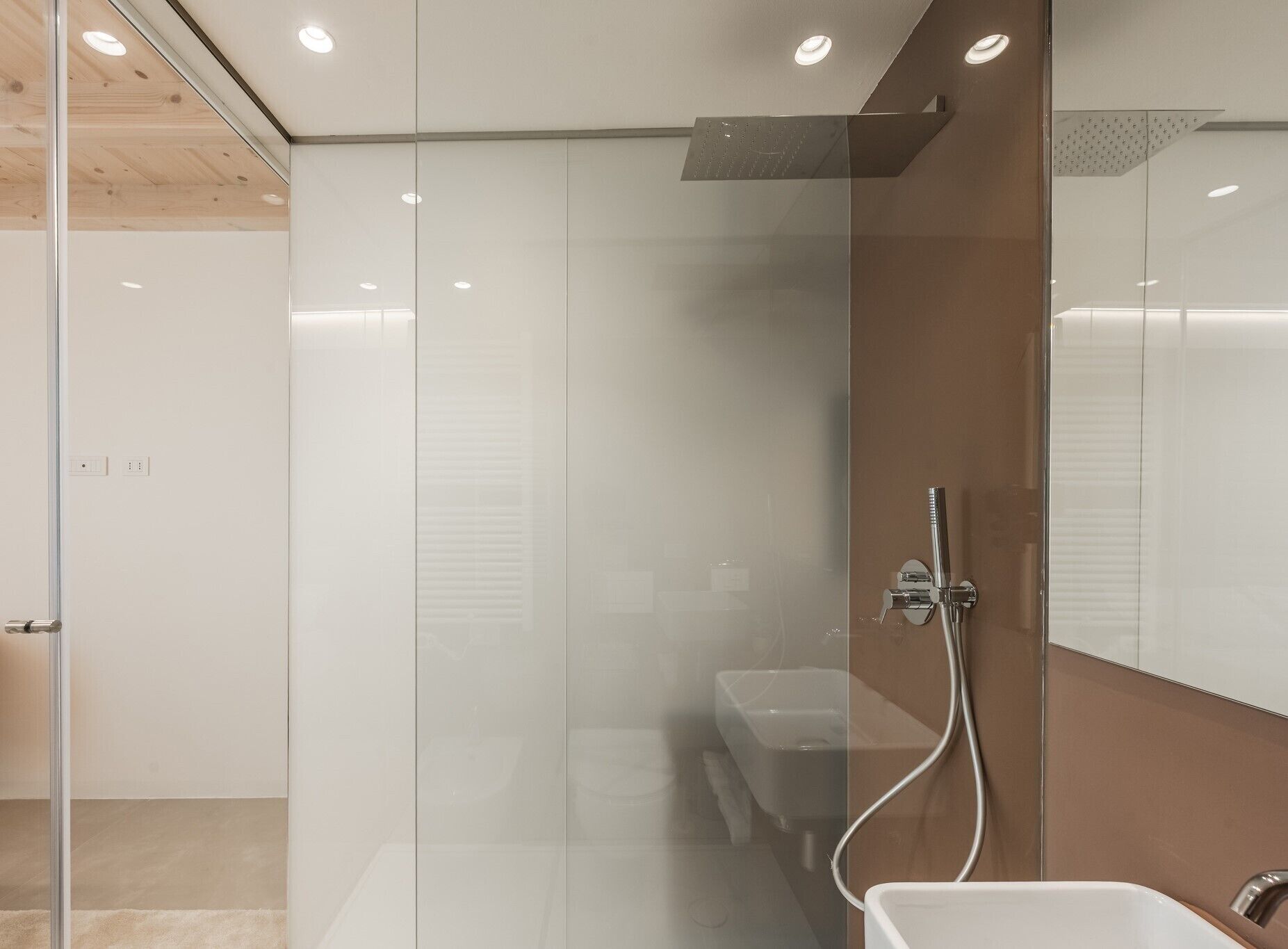 Een moderne badkamer met een glazen douchecabine, een witte wastafel en een houten plafond.