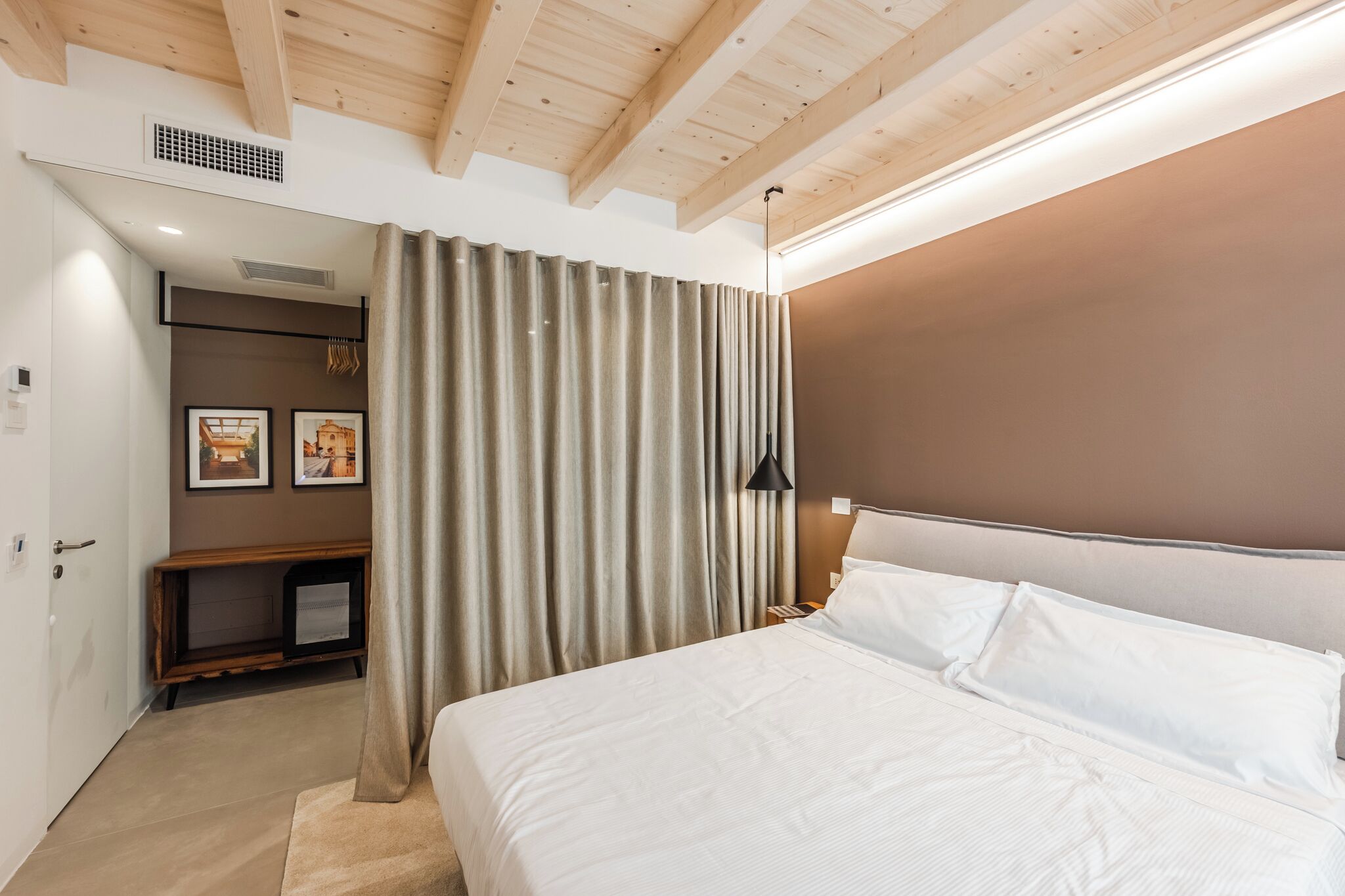 A bedroom with a large bed, a headboard, a bedside table, a lamp, and a curtain.