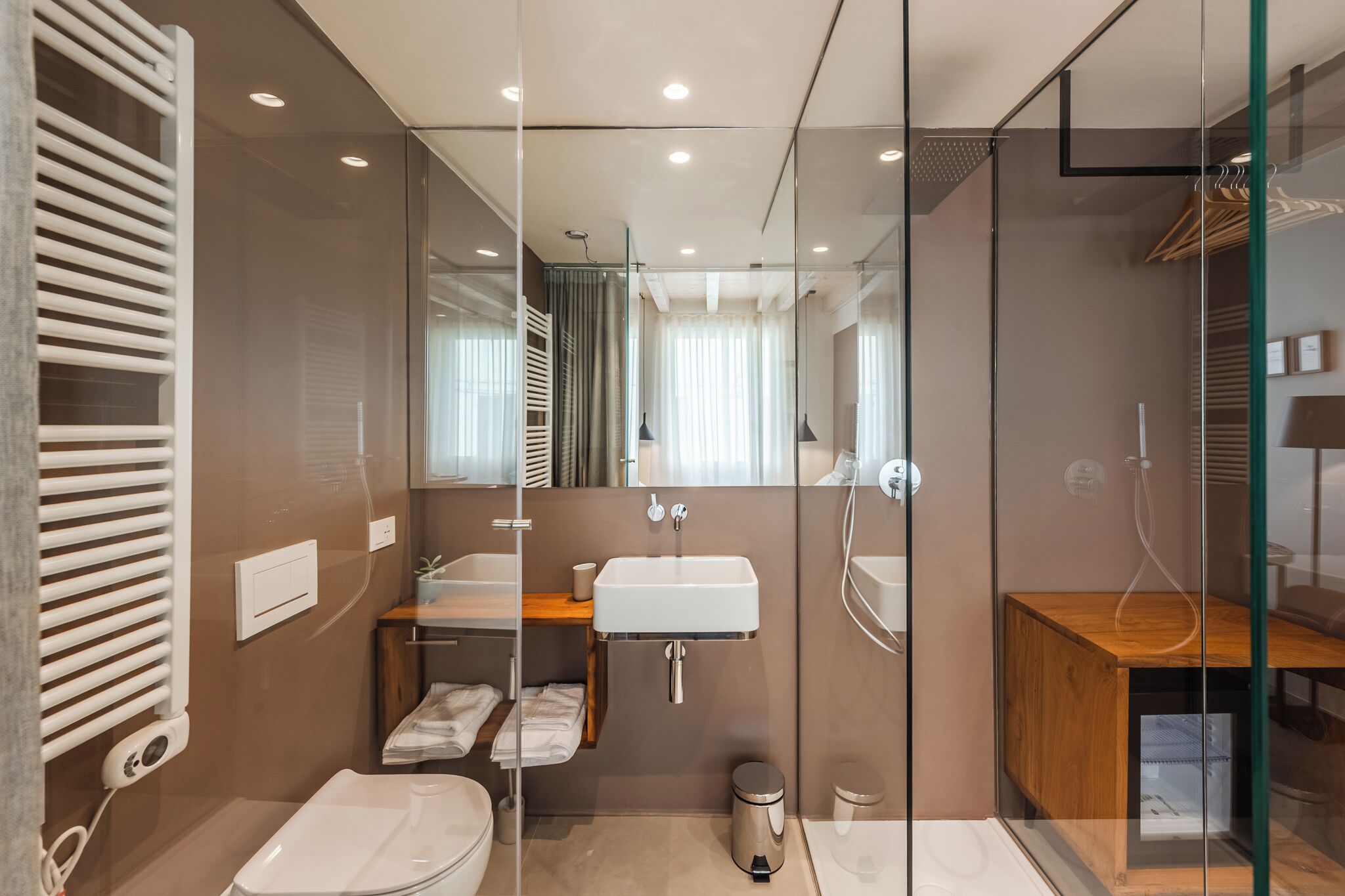 A modern bathroom with a glass shower enclosure, a white sink, and a wooden vanity.