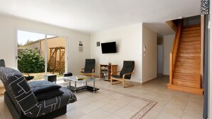 A living room with a sofa, chairs, a coffee table, a TV, and a staircase. - Family House with 4 Bedrooms for 13 Guests (La Plaine-sur-Mer)