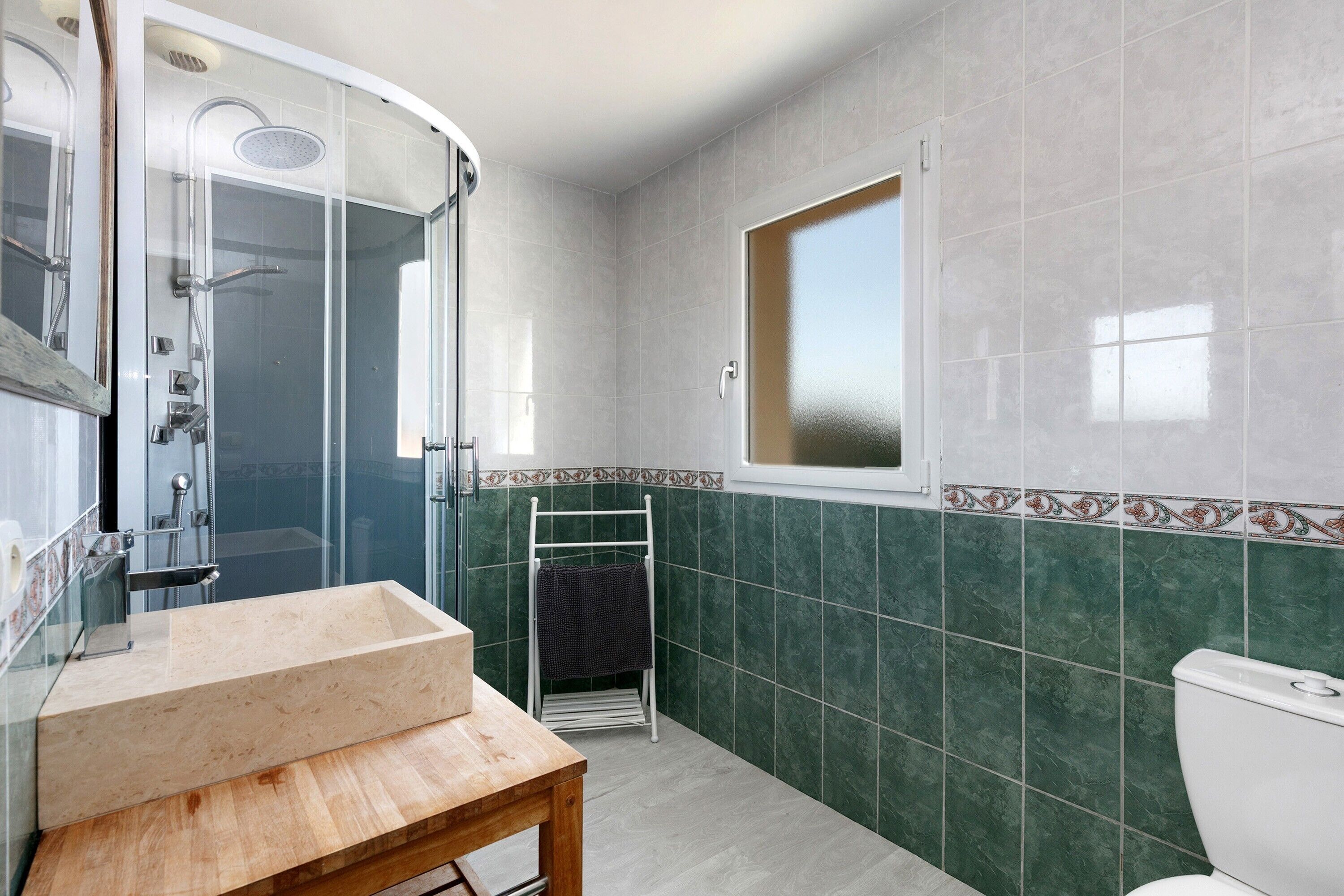 A bathroom with a glass-enclosed shower, a wooden vanity, a towel rack, and a toilet.