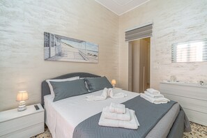 Een slaapkamer met een bed, kussens, een schilderij, een nachtkastje, een lamp, een dressoir en een spiegel.