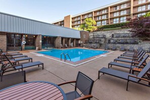 A pool area with lounge chairs and a table, surrounded by a building with multiple floors and balconies.