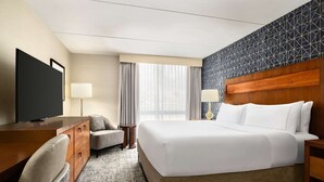 Habitación de hotel con cama, escritorio, silla, televisor y ventana con cortinas.