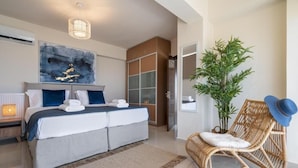 Ein Schlafzimmer mit einem Bett, einem großen abstrakten Gemälde, einem Kleiderschrank, einem Korbsessel und einem Blumentopf.