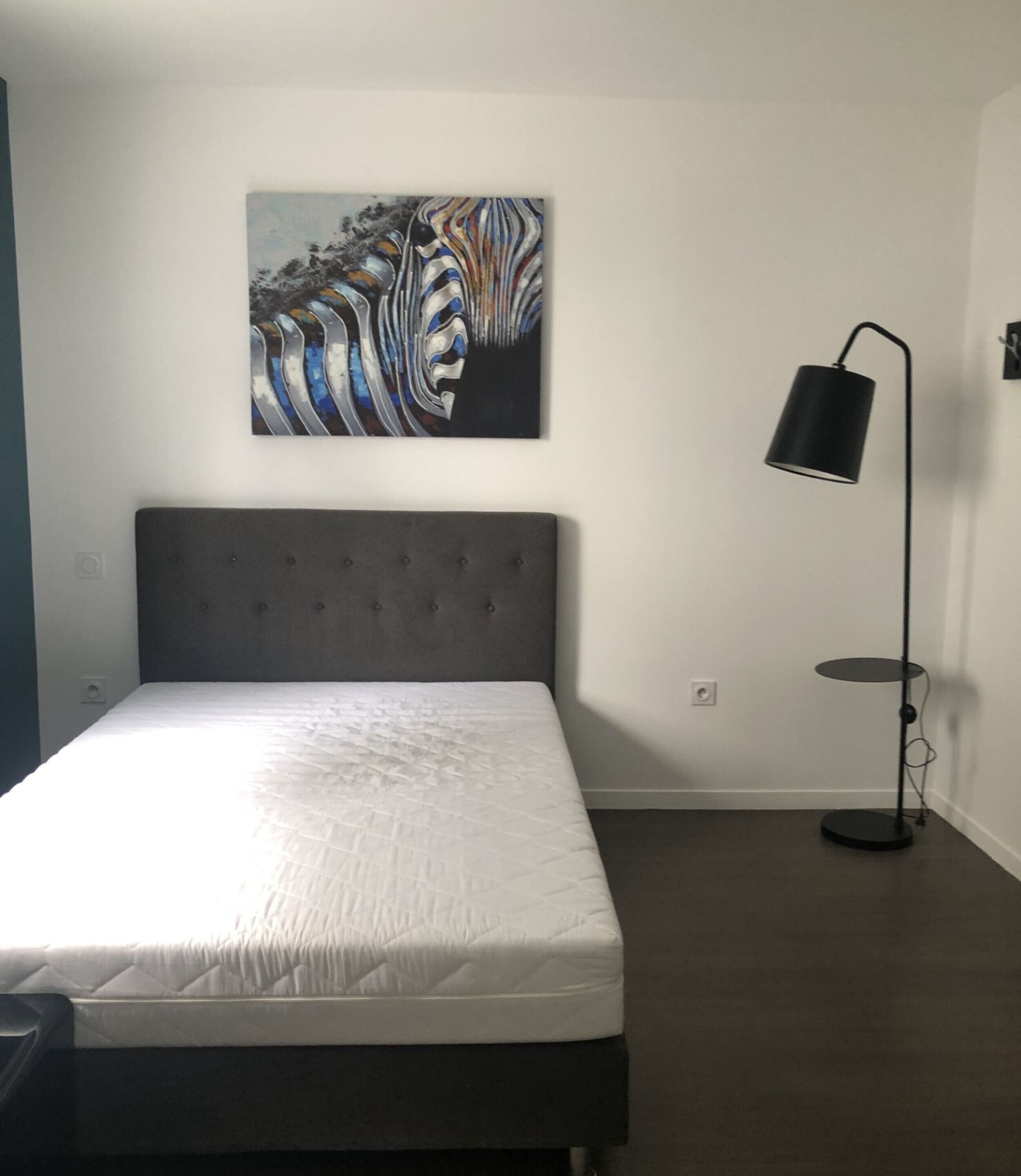 A bedroom with a bed, a headboard, a floor lamp, and a painting on the wall.