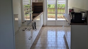 A kitchen with white cabinets, a countertop, and a window with blinds. - Family home 500 m from the beach (Saint-Marcouf)