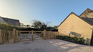 A gravel driveway leading to a wooden gate, a building with a triangular roof, and a signpost with a fish symbol. - Family home 500 m from the beach (Saint-Marcouf)