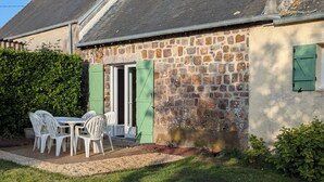 A stone building with a door and windows, a table with chairs, and a hedge. - Family home 500 m from the beach (Saint-Marcouf)