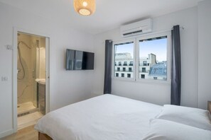 Ein Schlafzimmer mit einem Bett, einem Fernseher, einem Fenster mit Vorhängen, einer Klimaanlage und einer Dusche.