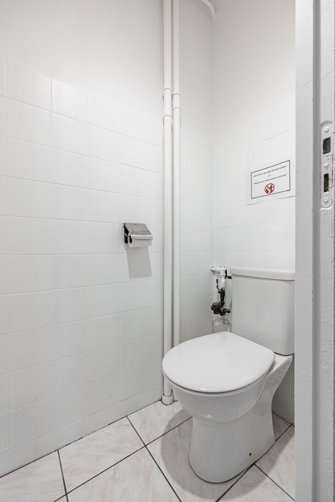 Un baño con azulejos blancos, un inodoro, un dispensador de toallas de papel y un cartel de prohibido tirar basura.