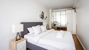 A modern hotel room with a large bed, a bedside table, a nightstand, a mirror, and a wardrobe. - Mobility Lease - Porte Dauphine - 1 large bedroom (Paris)