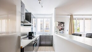 A modern kitchen with a built-in oven, a coffee machine, and a window with a view of buildings. - Mobility Lease - Porte Dauphine - 1 large bedroom (Paris)