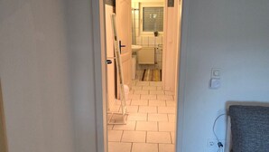 Un couloir avec une porte donnant sur une salle de bain, un radiateur et une prise électrique sur le mur.