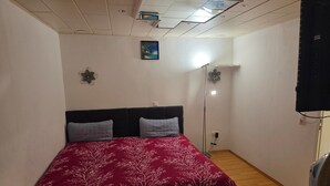 Une chambre à coucher comprenant un lit, une table de chevet, un téléviseur fixé au mur, un luminaire au plafond et un petit tableau accroché au mur.