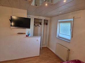 Ein Zimmer mit Wandfernseher, Fenster mit Blick, Heizkörper und Holzboden.