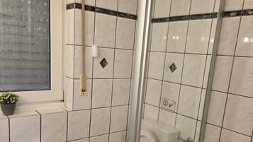Ein Badezimmer mit Dusche, Toilette und einem Fenster mit Pflanze.