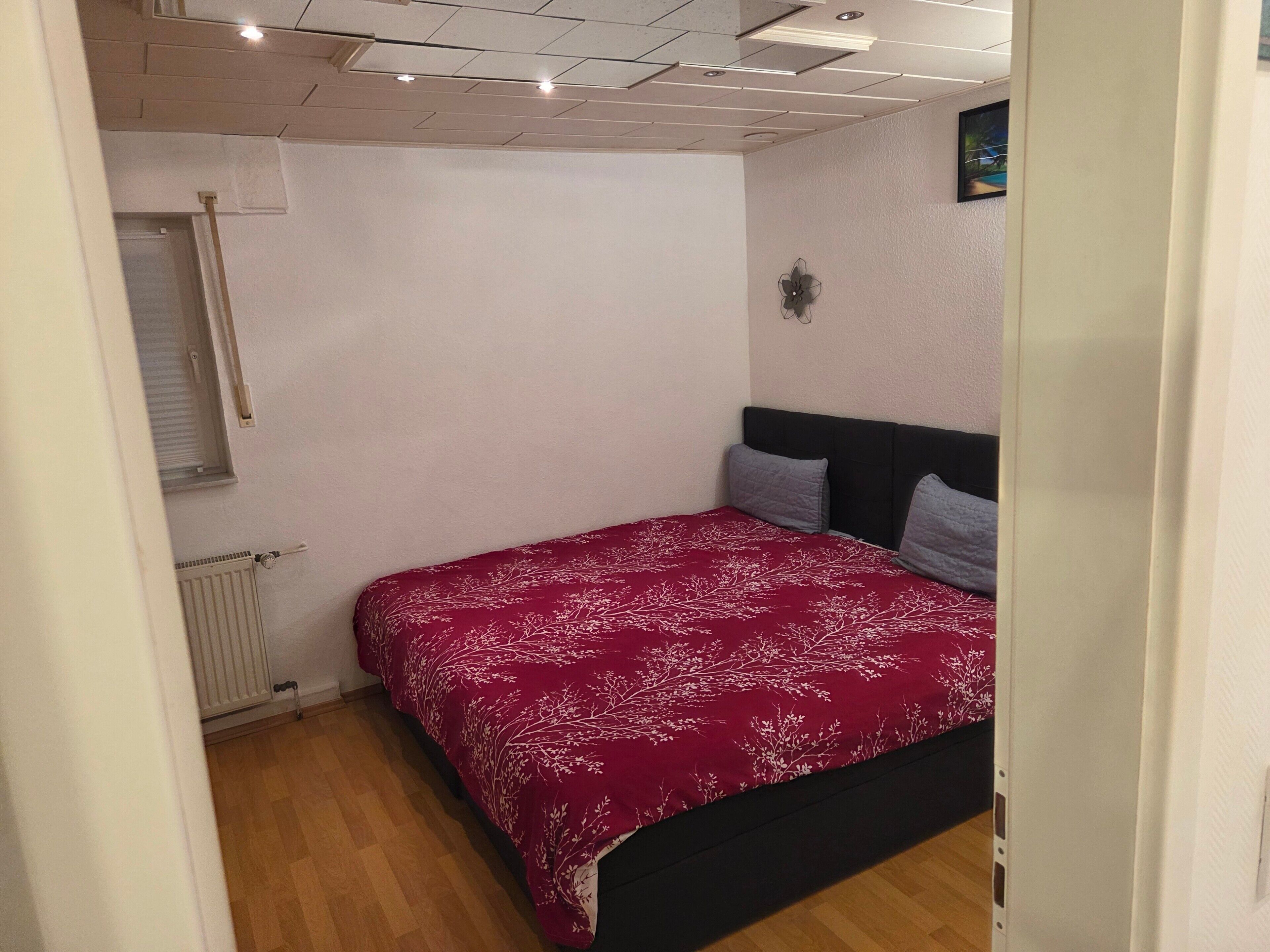 A bedroom with a bed, a radiator, a window with blinds, and a ceiling with recessed lighting.