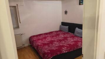A bedroom with a bed, a radiator, a window with blinds, and a ceiling with recessed lighting.
