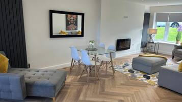 A modern living room with a fireplace, a dining area with a glass table, and a sofa.