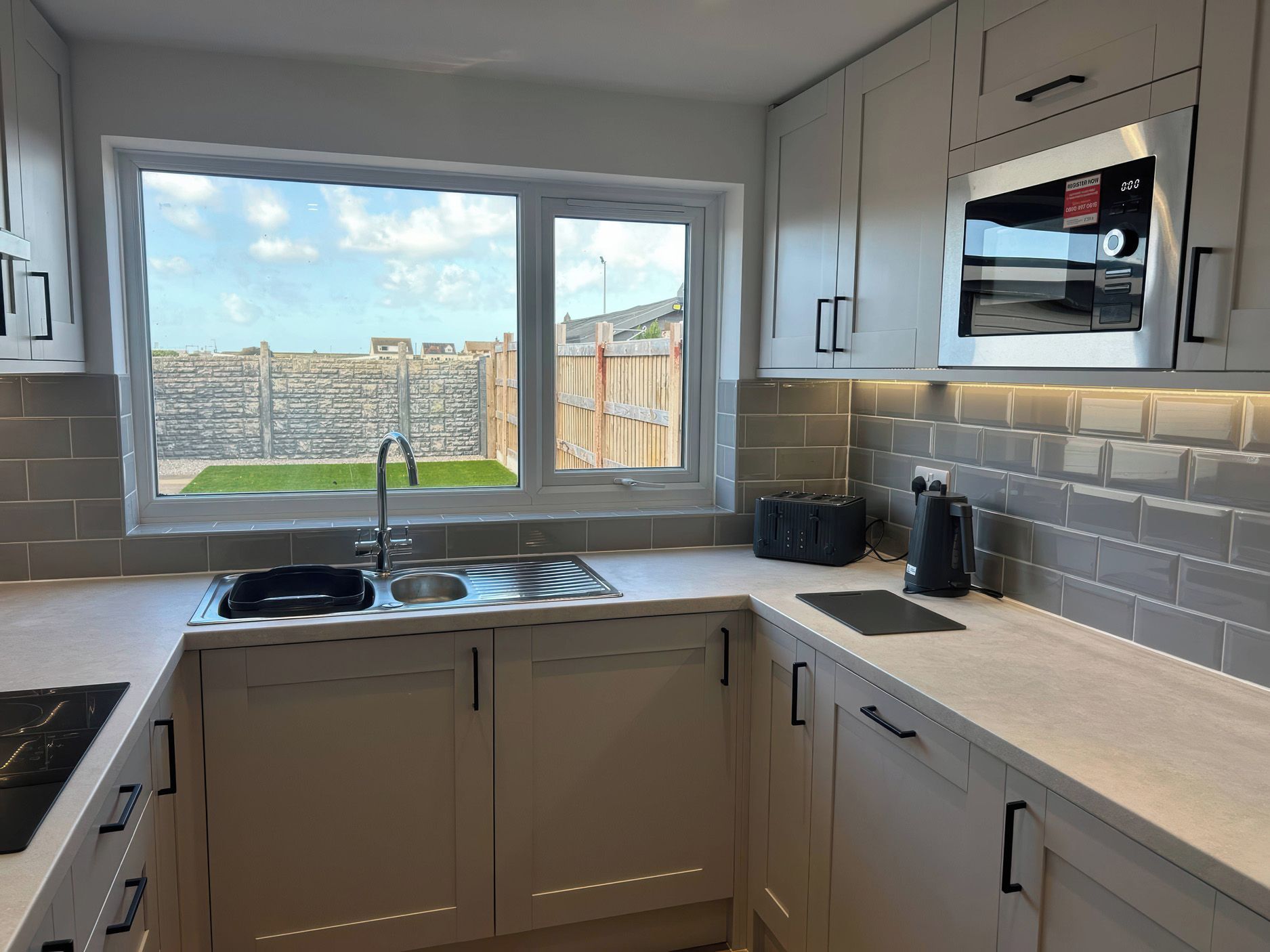 A modern kitchen with a built-in oven, a window with a view of a garden, and a stone wall outside.