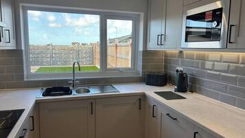 A modern kitchen with a built-in oven, a window with a view of a garden, and a stone wall outside.