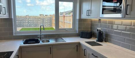 A modern kitchen with a built-in oven, a window with a view of a garden, and a stone wall outside.
