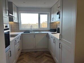 A compact kitchen with white cabinets, a double sink, and a view through the window. - 21 Bastion Gardens (Prestatyn)