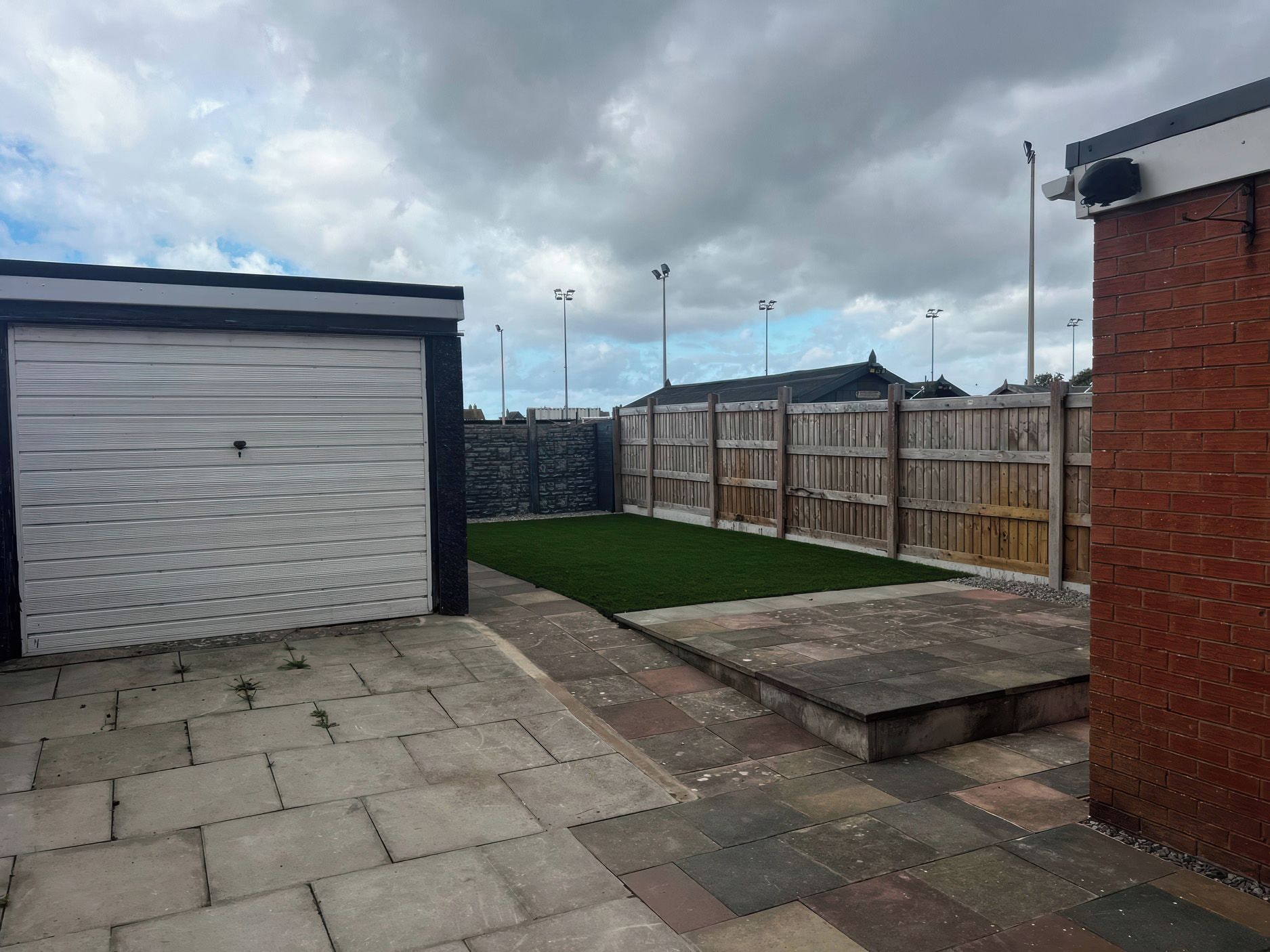 A garage with a closed white door, a paved patio area, and a fenced yard with a grassy patch.