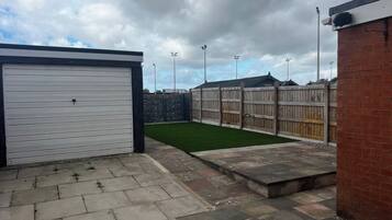 A garage with a closed white door, a paved patio area, and a fenced yard with a grassy patch.