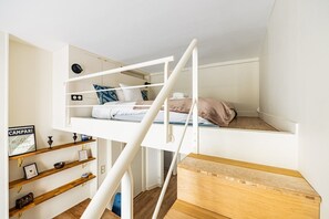 Ein Etagenbett mit weißem Gestell, ein Holztisch und Regale mit verschiedenen Gegenständen.
