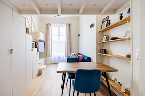 Ein gemütlicher Wohnraum mit Esstisch, blauen Stühlen, einer Couch mit bunten Kissen und integrierten Regalen.