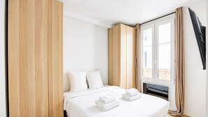 A bedroom with a bed, white bedding, a wooden wardrobe, a window with curtains, and a flat-screen TV. - 2 People #1 Bedroom #Invalides #Eiffel Tower #Paris 07 (Paris)
