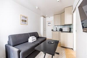 Ein kompakter Wohnraum mit einer Couch, einem kleinen Tisch, einer Küchenzeile und einem Fernseher.