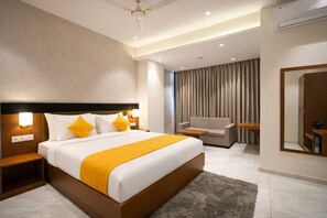 A modern hotel room with a large bed, a sofa, a desk, and a mirror.