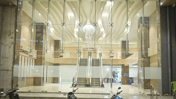 A modern building with glass walls, a central staircase, and a chandelier. - Solasta Stays & Banquets - Wakad (Tathawade)