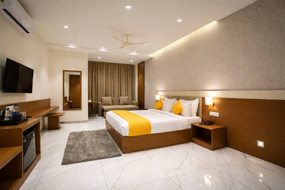 Una habitación de hotel con cama, mesitas de noche, televisor, escritorio, sofá y ventilador de techo.