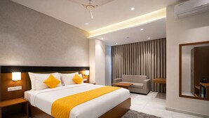 A modern hotel room with a large bed, bedside tables, a sofa, a mirror, and a ceiling fan. - Solasta Stays & Banquets - Wakad (Tathawade)