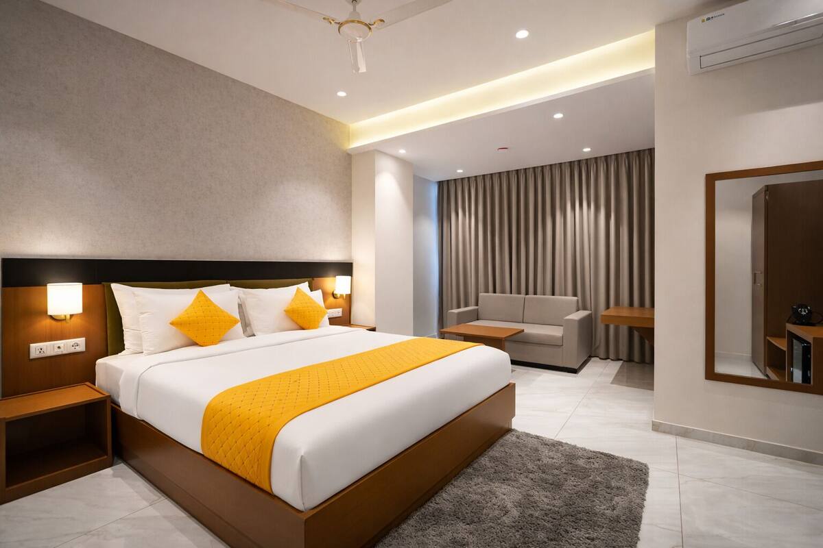 Una habitación de hotel moderna con una cama grande, mesitas de noche, un sofá, un espejo y un ventilador de techo.